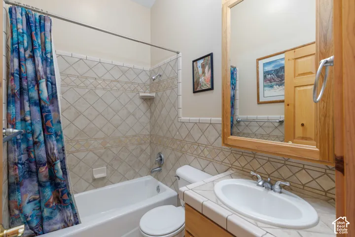 Bathroom featuring a ceramic tile vanity with an oval sink, a wood-framed mirror, a toilet, and a bathtub with tiled surround