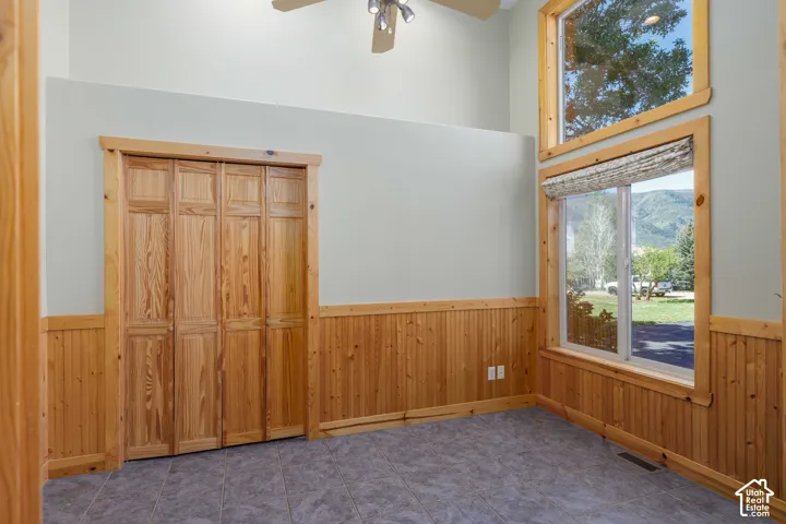 Vaulted ceiling with a ceiling fan, wood-paneled wainscoting, wood-finish bi-fold closet doors, tile flooring, and multiple windows with wood trim