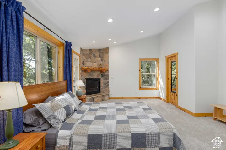 Corner stone fireplace with wood mantel, vaulted ceiling with recessed lighting, wood-trimmed windows, and light-toned carpeting