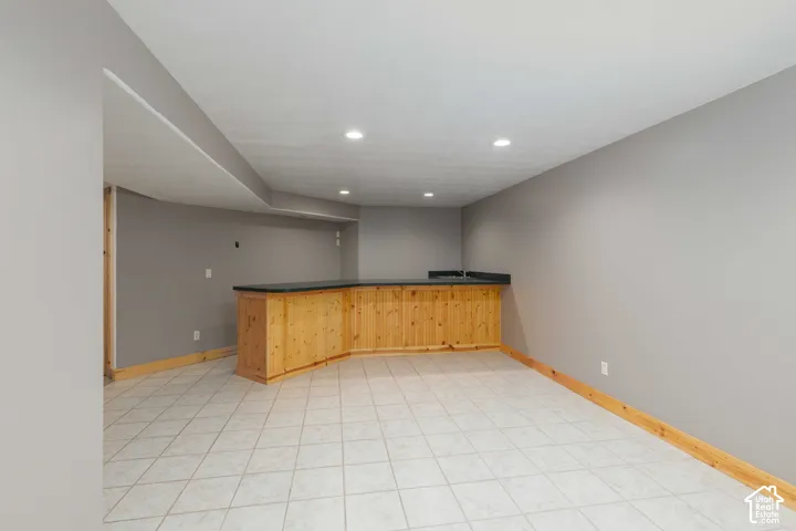 Tile flooring, recessed lighting, and a built-in wood-finish bar with a dark countertop