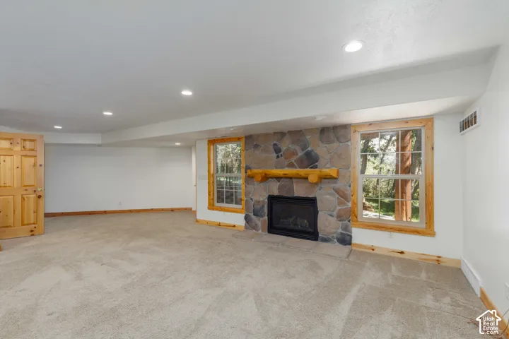 Stone-clad fireplace with a wood mantel, two windows with wood trim, recessed ceiling lighting, and carpet flooring