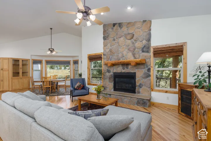 Expansive living area with vaulted ceilings, hardwood flooring, a stone-faced fireplace with a log mantel, and built-in cabinetry