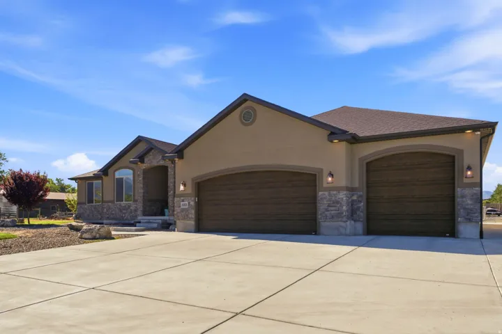 Stucco and stone exterior with arched garage doors, a concrete driveway, and a covered entry