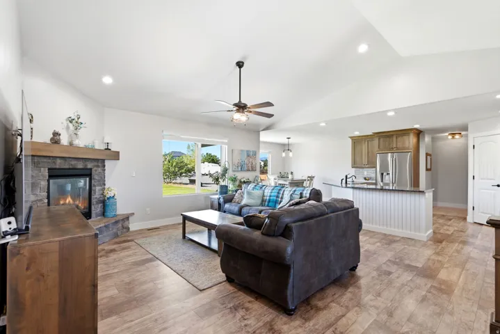 Vaulted ceiling with recessed lighting, stone-clad fireplace with wood mantle, wood-finish flooring, kitchen with stainless steel appliances, and a breakfast bar with beadboard paneling