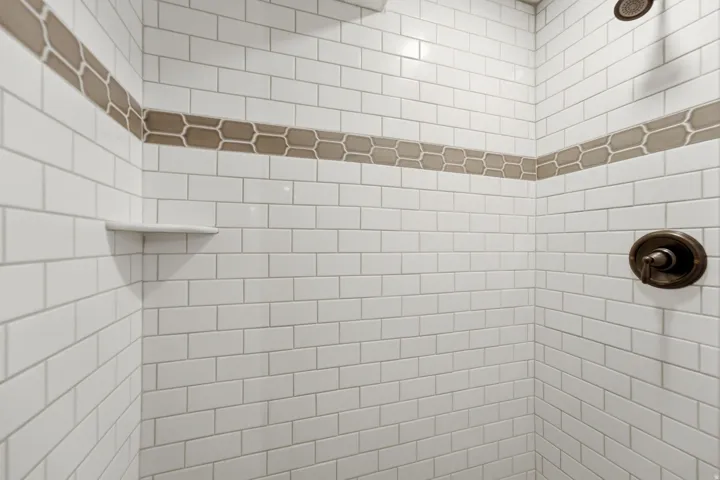 White subway tile shower enclosure with a decorative hexagon tile accent band, integrated corner shelf, and bronze-finish fixtures