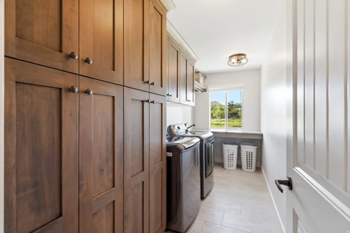 Laundry area featuring extensive wood-finish cabinetry, a built-in countertop, a window, and tile flooring