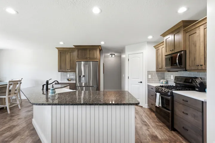 Kitchen with wood-finish flooring, recessed lighting, and a kitchen island featuring a beadboard base and dark countertop