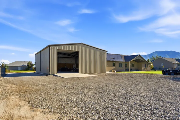Large gravel-surfaced area featuring a metal-sided outbuilding with an open bay