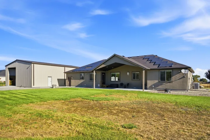 Expansive yard featuring a large detached metal-sided outbuilding, a covered patio, and rooftop solar panels