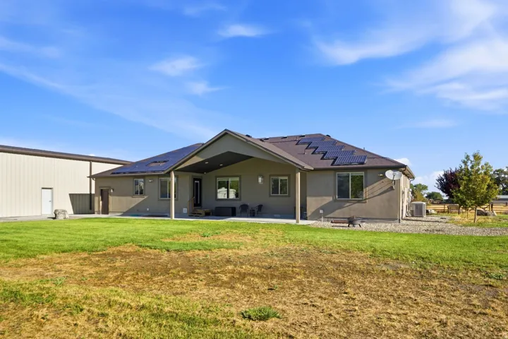 Rear exterior with covered patio, solar panels, stucco siding, and a detached outbuilding