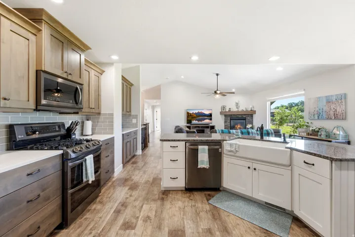 Open-concept kitchen with wood-finish flooring, white and wood-tone cabinetry, a farmhouse sink, and granite countertops