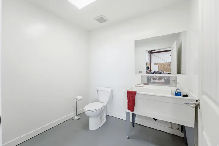 White walls with a utility sink, wall-mounted mirror, and a ceiling-mounted light fixture