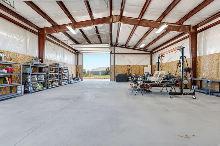 Spacious utility building featuring a concrete floor, exposed steel beam construction, overhead lighting, and a large roll-up door
