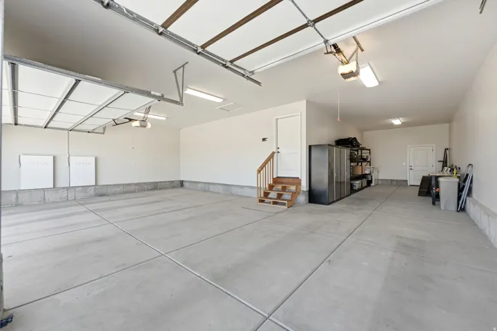 Spacious garage with exposed overhead garage door mechanisms, concrete flooring, and multiple ceiling-mounted light fixtures