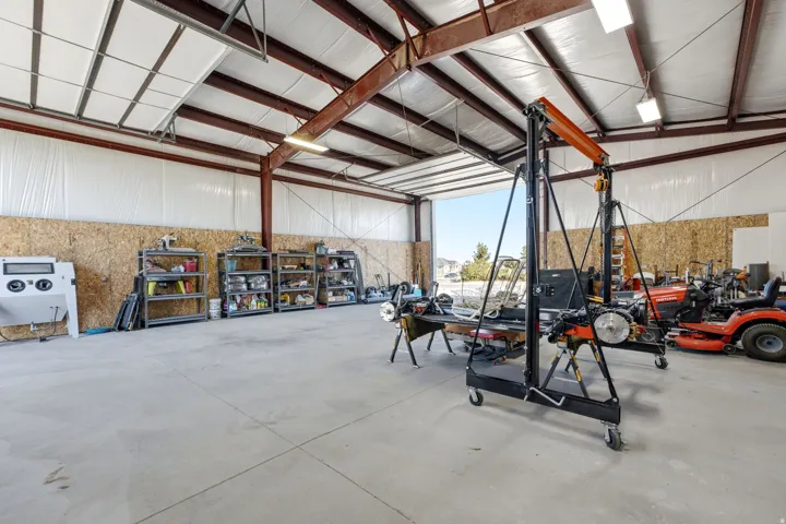 Spacious workshop featuring a concrete floor, exposed structural beams, ceiling-mounted lighting, and a large overhead door