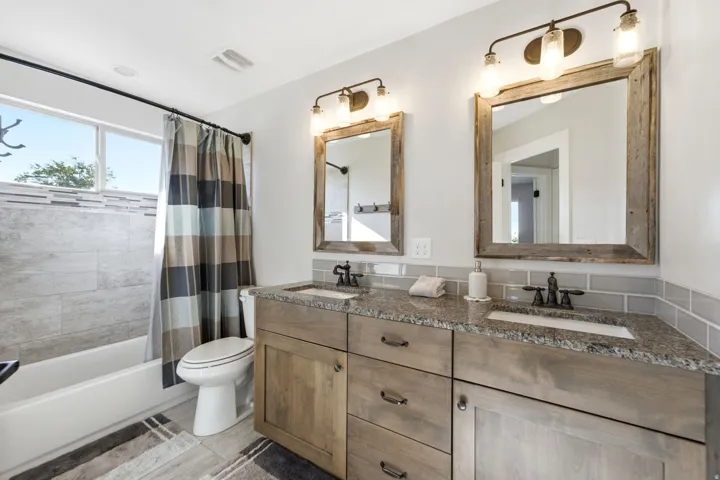 Dual vanity with granite countertops, wood-finish cabinetry, and framed mirrors