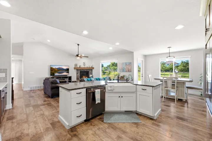 Open-concept living space featuring wood-finish flooring, a kitchen island with integrated dishwasher, a fireplace with stone surround, and vaulted ceilings