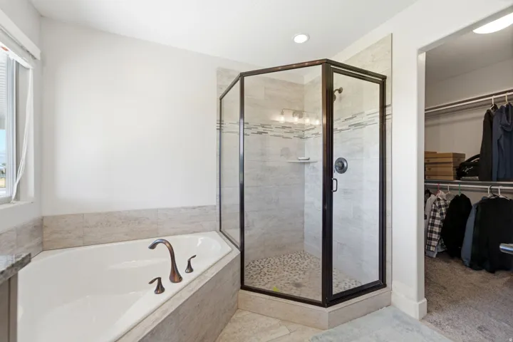 Corner soaking tub with bronze-finish fixtures, a glass-enclosed shower with pebble-finish flooring, tiled walls, and a recessed ceiling light