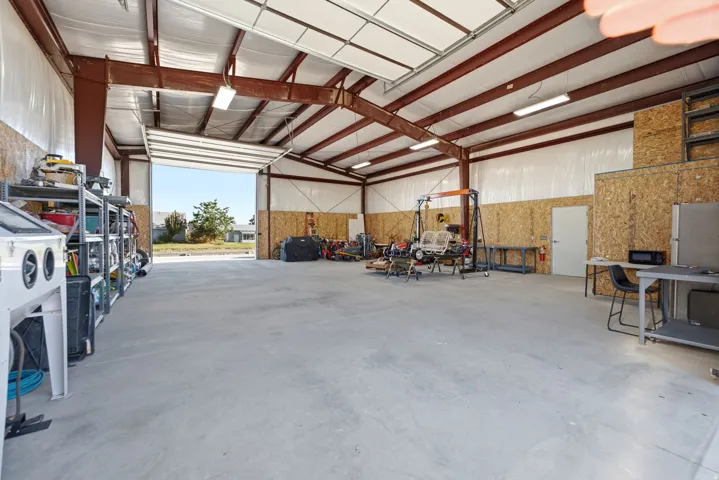 Expansive open interior space with a concrete floor, exposed structural beams, a large roll-up door, and white interior walls