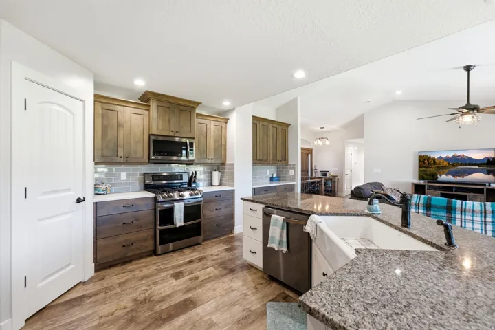 Contemporary kitchen featuring wood-finish flooring, stainless steel appliances, a subway tile backsplash, and a large kitchen island with a farmhouse sink