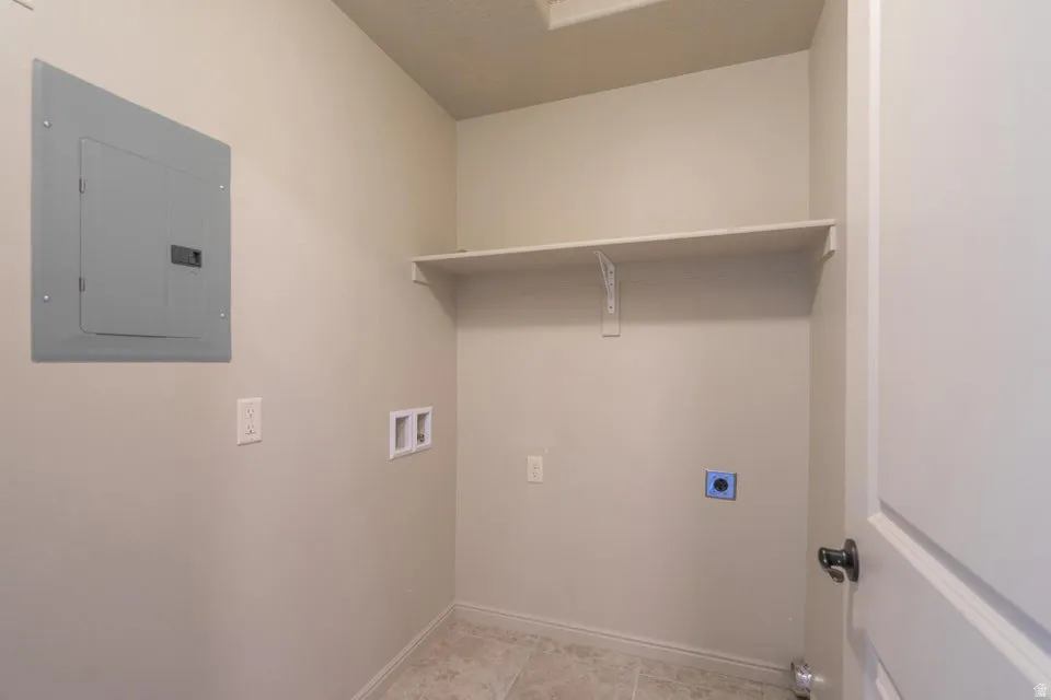 Utility area featuring a wall-mounted electrical panel, electrical outlets, and plumbing hookups
