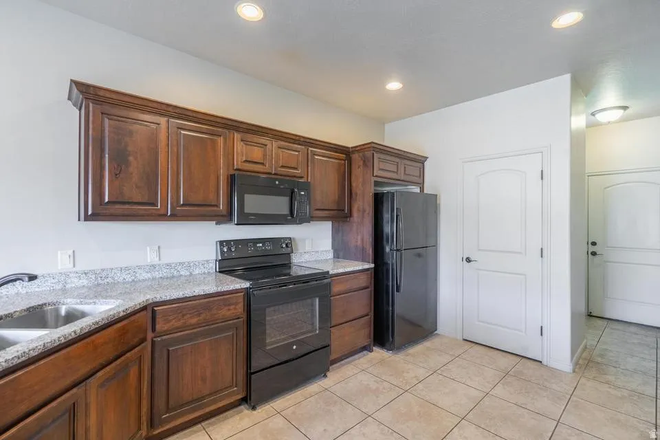 Kitchen featuring dark wood cabinetry, light speckled countertops, and black appliances