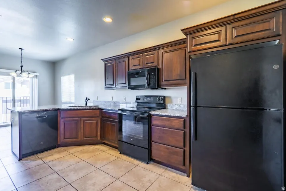 Kitchen featuring dark wood cabinetry, light speckled countertops, and black appliances