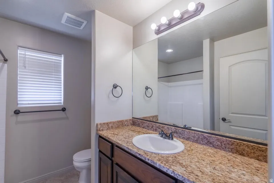 Bathroom featuring a vanity with a granite-style countertop, integrated sink, and an expansive mirror