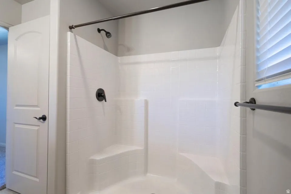 Shower with integrated seating, white subway tile surround, dark bronze fixtures, and window with privacy blinds
