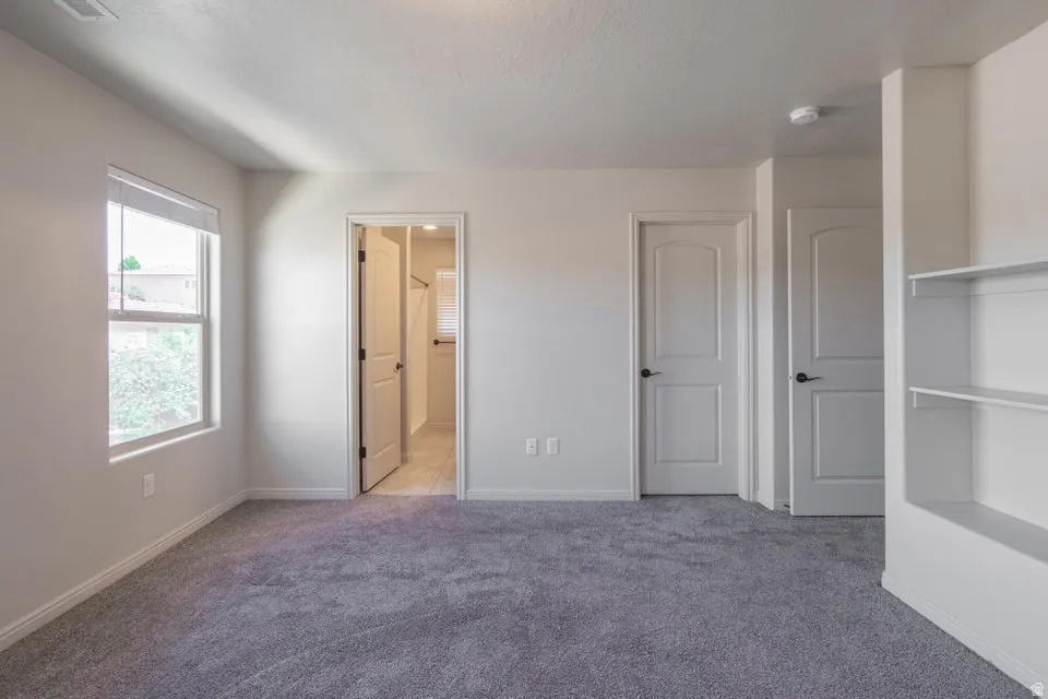 Carpeted room featuring a single window, built-in shelving, and multiple arched panel doors