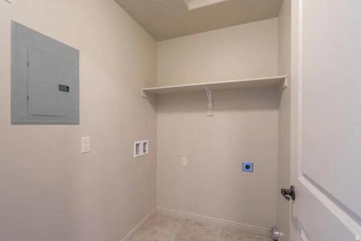 Utility area featuring a wall-mounted electrical panel, electrical outlets, and plumbing hookups