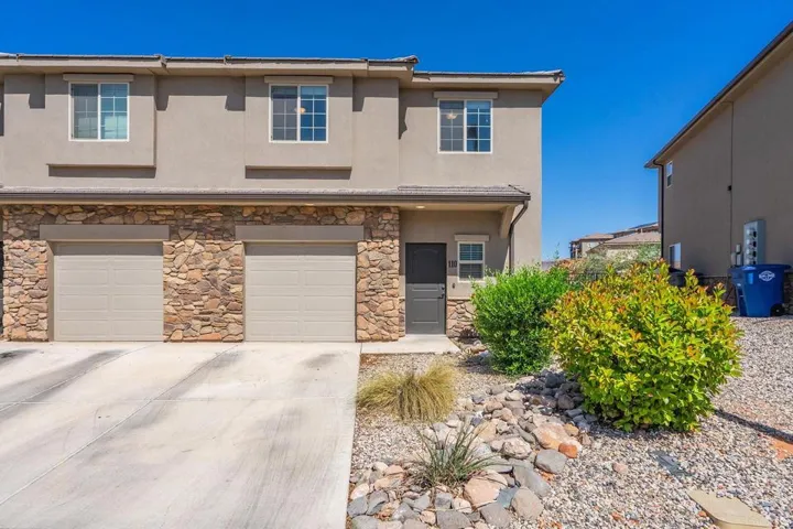 Stucco exterior featuring a stone-clad lower level, two garage doors, and a front entry