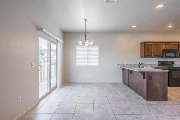 Open-concept kitchen and dining area featuring tile flooring, a kitchen island with stone countertops, wood cabinetry, and a glass sliding door opening to a balcony