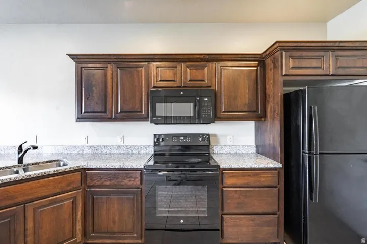Kitchen featuring dark wood cabinetry, speckled countertops, stainless steel double basin sink with a matte black faucet, and black appliances including a microwave, electric range, and refrigerator