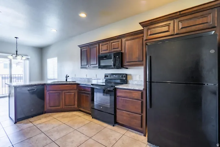 Kitchen featuring dark wood cabinetry, light speckled countertops, and black appliances