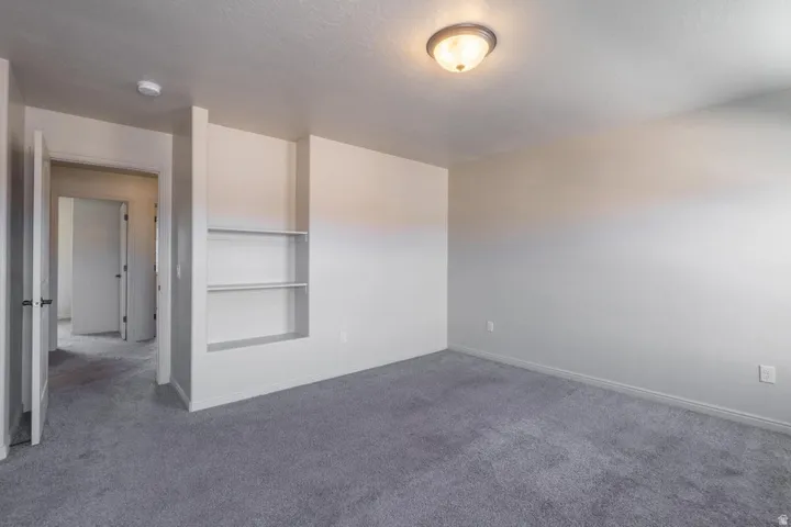 Spacious room featuring neutral-toned walls, grey carpeting, and recessed built-in shelving