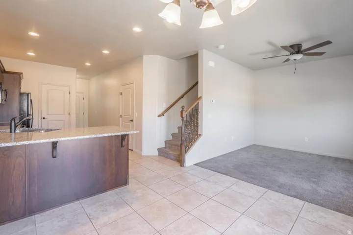 Open-concept kitchen and living area featuring a large island with granite-style countertop, dark wood-finish cabinetry, tile flooring, and a ceiling fan in the living space