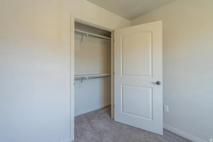 Closet with shelving and hanging rod, featuring neutral wall paint, carpeted flooring, a two-panel interior door with a brushed nickel handle, and crisp white baseboards
