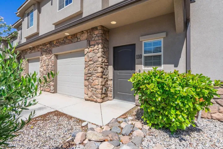 Stucco exterior featuring stone veneer accents, two attached garage doors, and a dark entry door with transom window