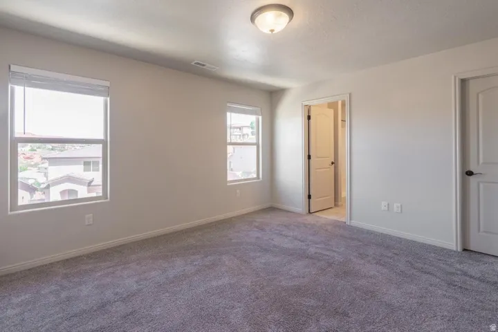 Spacious room featuring neutral-toned walls, plush carpet flooring, two windows with blinds, and white panel doors