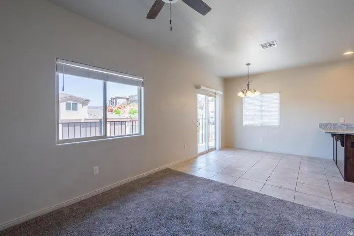 Open concept living area featuring a ceiling fan, window with blinds, sliding glass door, and a three-light chandelier