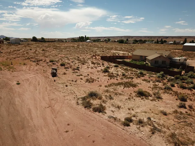 Expansive desert landscape featuring a single-story dwelling with a surrounding privacy fence and a gravel driveway