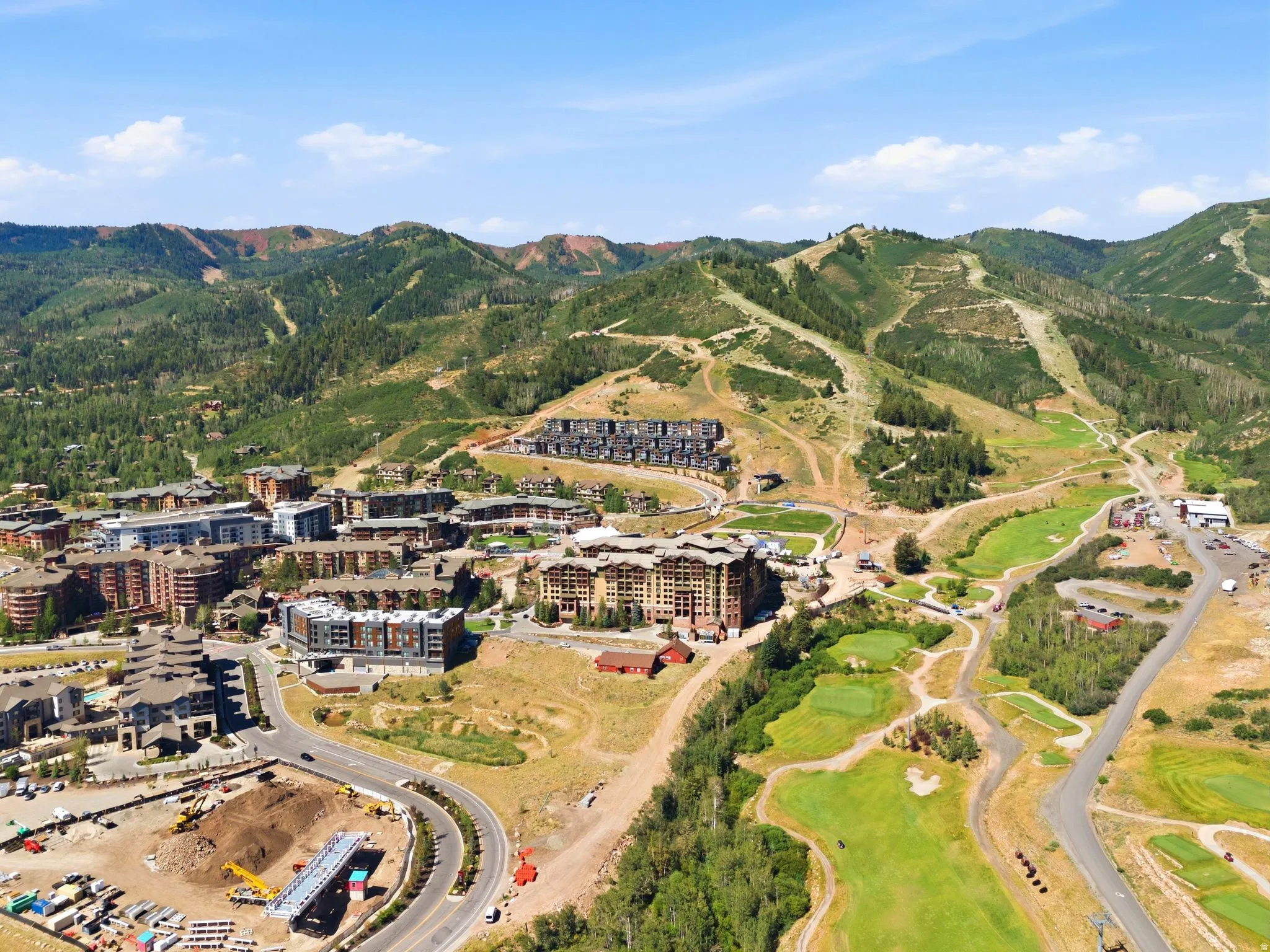 Expansive aerial capturing a mountain community featuring multiple residential buildings, verdant golf course fairways, and a winding paved road system