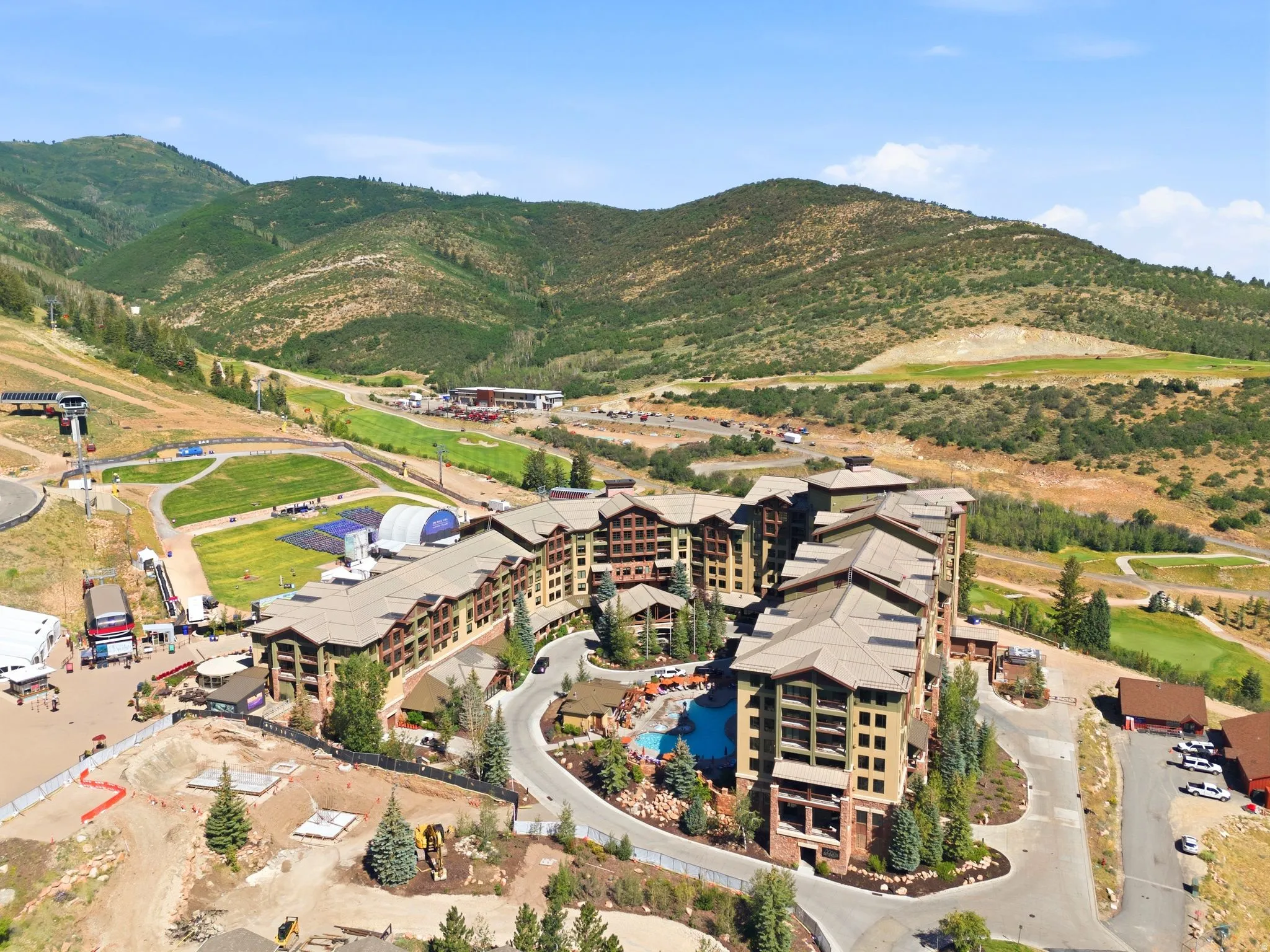 Multi-story property featuring a large outdoor pool, extensive hardscaping, and surrounding mature trees