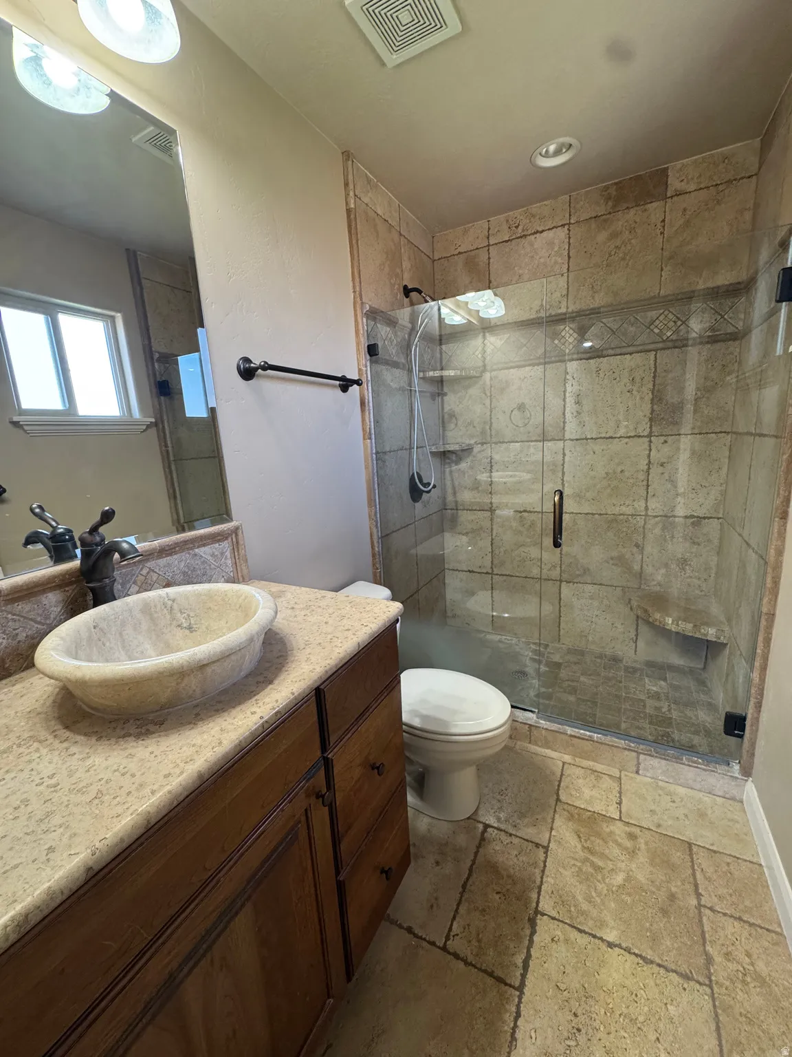 Bathroom featuring a stone vessel sink, dark wood-finish vanity with ample storage, and a stand-up shower with glass enclosure