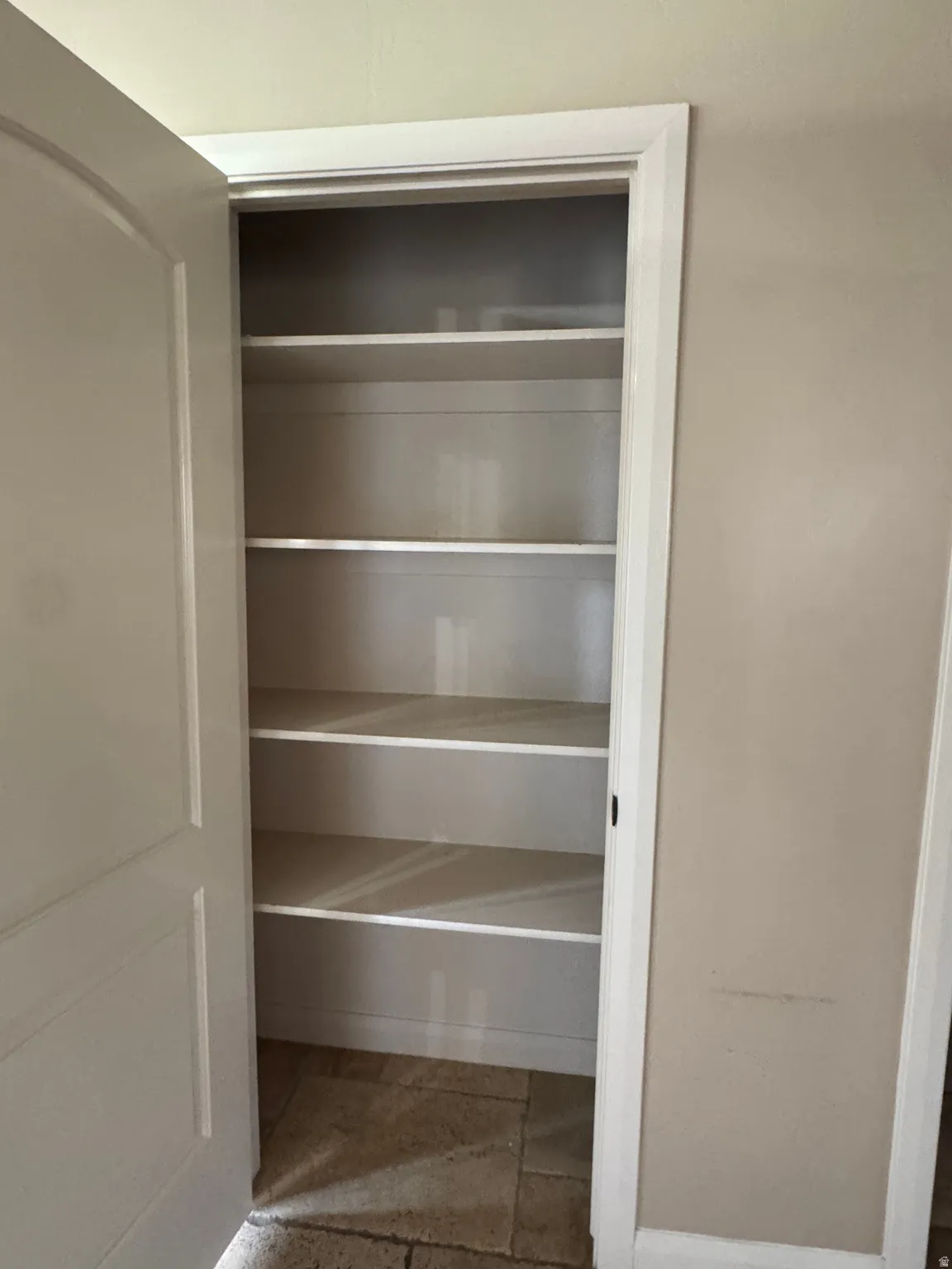 Spacious built-in closet with multiple white shelves, a neutral wall finish, and tile flooring