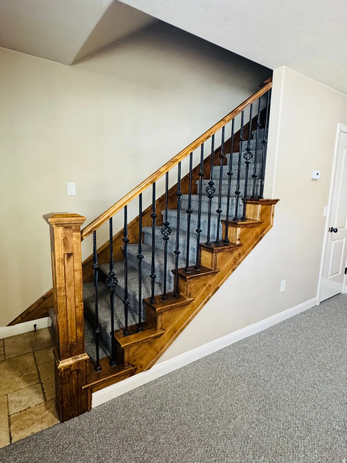 Staircase featuring wood treads and handrail, wrought iron balusters with decorative elements, and a carpeted runner