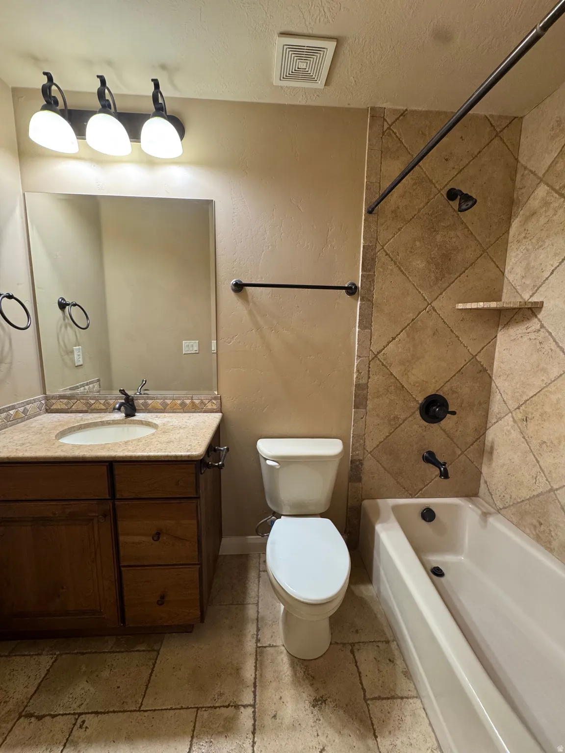 Bathroom featuring a wood-finish vanity with a stone countertop and integrated sink, complemented by a large mirror and three-light fixture