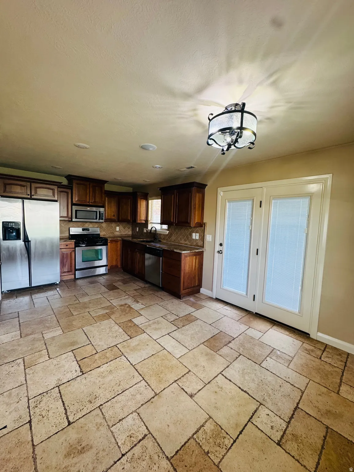 Kitchen area featuring a mosaic tile floor, warm wood cabinetry, stainless steel appliances, and French doors