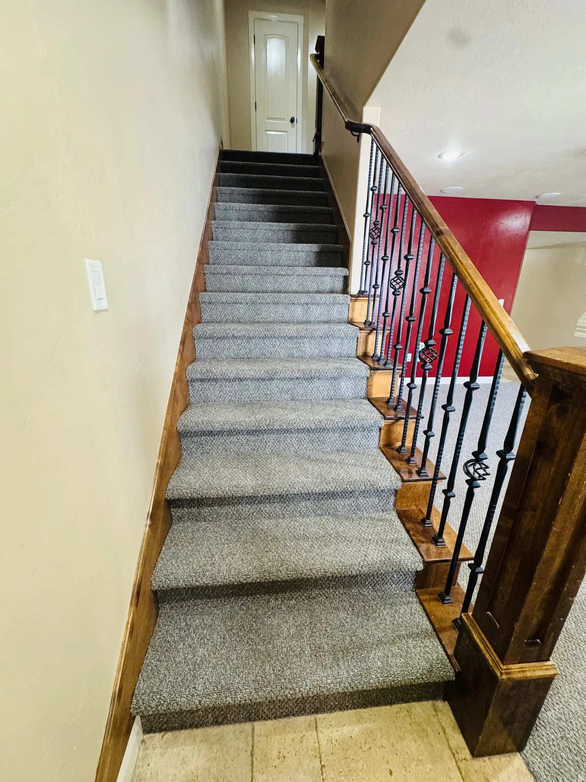 Staircase featuring wood handrail, wrought iron balusters, and grey carpeted treads